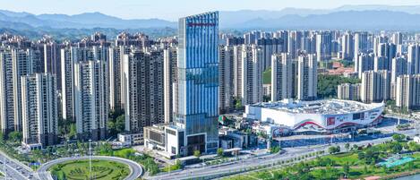 Un edificio alto con fachada de vidrio moderna, rodeado por una zona urbana densa con edificios residenciales elevados.