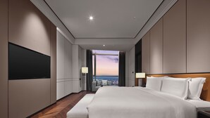 Moderni hotellihuone, jossa on suuri sänky, taulutelevisio, näkymä kaupunkiin ja puulattia.