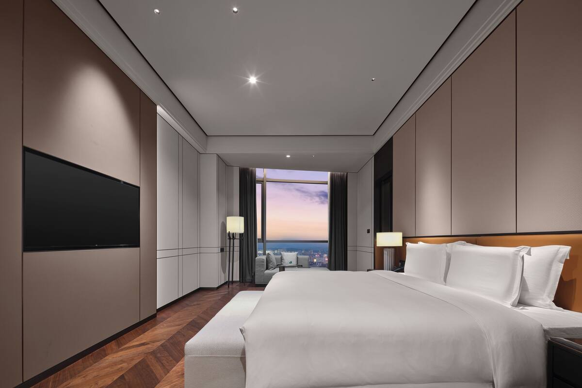 Une chambre d’hôtel moderne dotée d’un grand lit, d’un téléviseur à écran plat, d’une vue sur la ville et d’un plancher en bois.