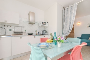 Une cuisine moderne avec des meubles blancs, une table à manger en verre et un canapé turquoise dans l’espace salon.