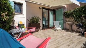 Un patio con mobiliario exterior, una parrilla y una planta en maceta.