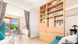 Una sala de estar moderna con un sofá, una zona de comedor con sillas, una estantería y vistas a través de un ventanal.