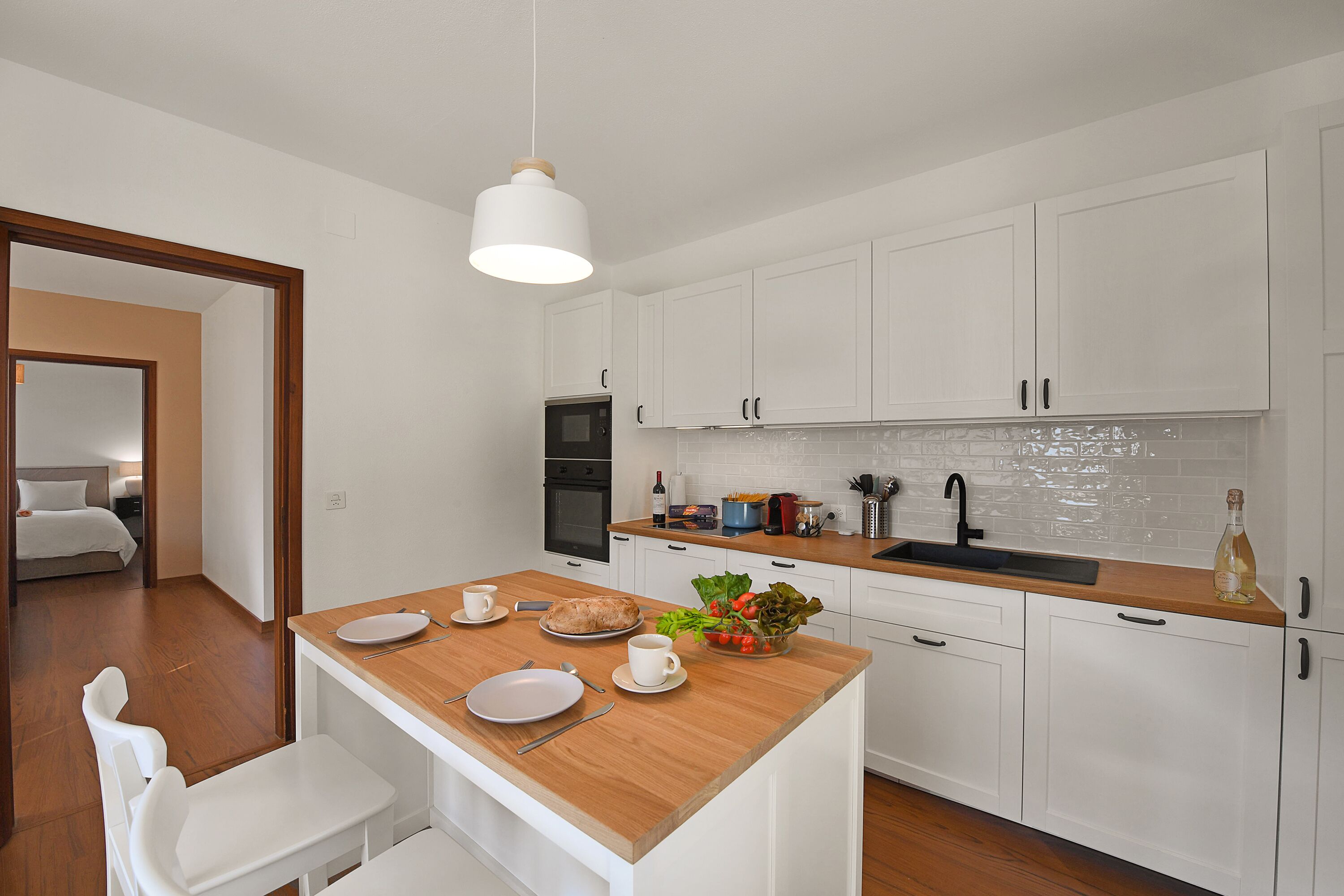 Eine moderne Küche mit weißen Schränken, einer Holz Arbeitsplatte und einer zentralen Kochinsel mit Essbereich.
