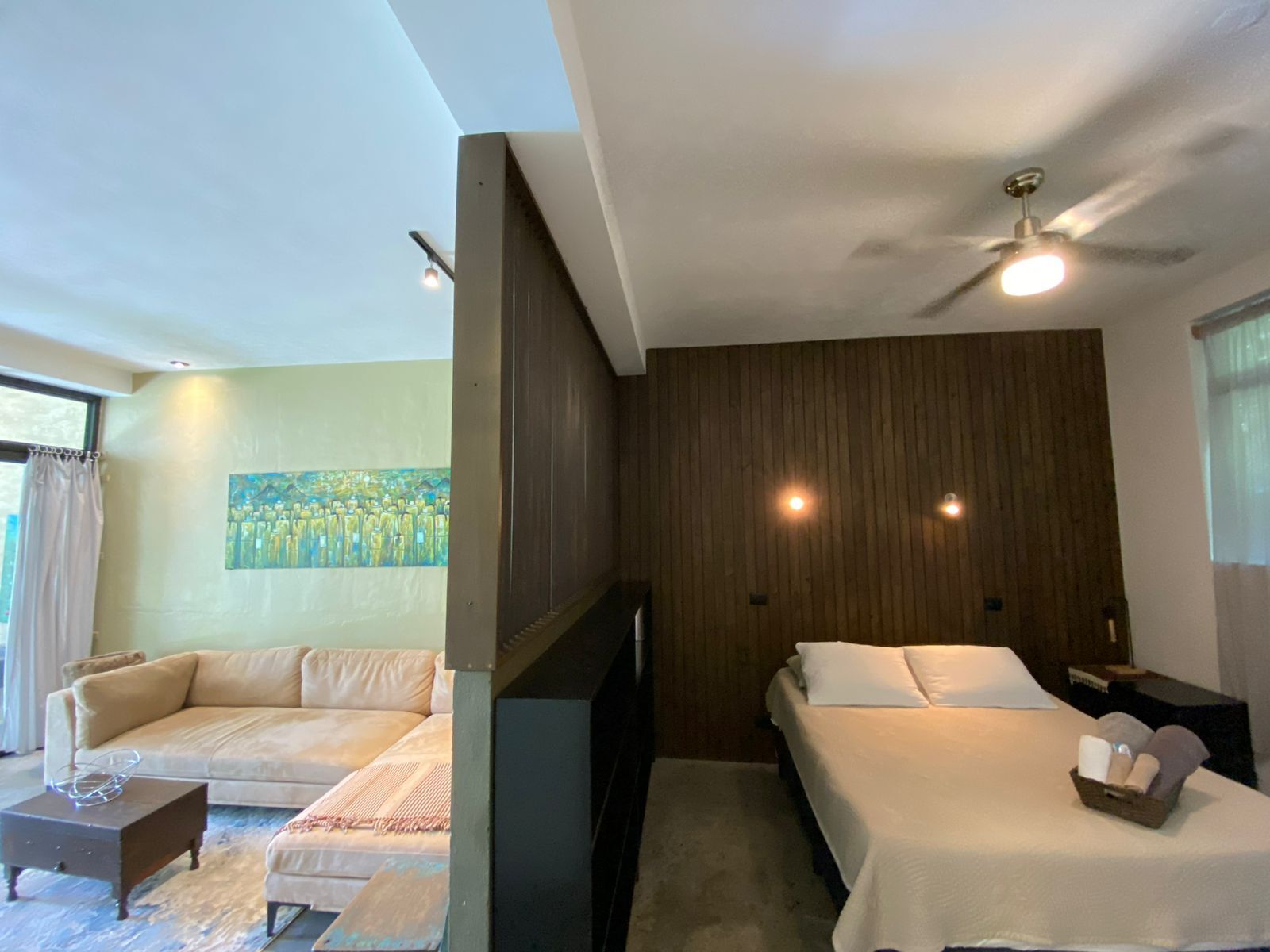 A modern hotel room with a sofa, two single beds, a small table, and a painting on the wall.