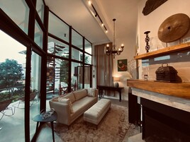 Una sala de estar moderna con ventanas amplias, una escalera, una araña y una chimenea.