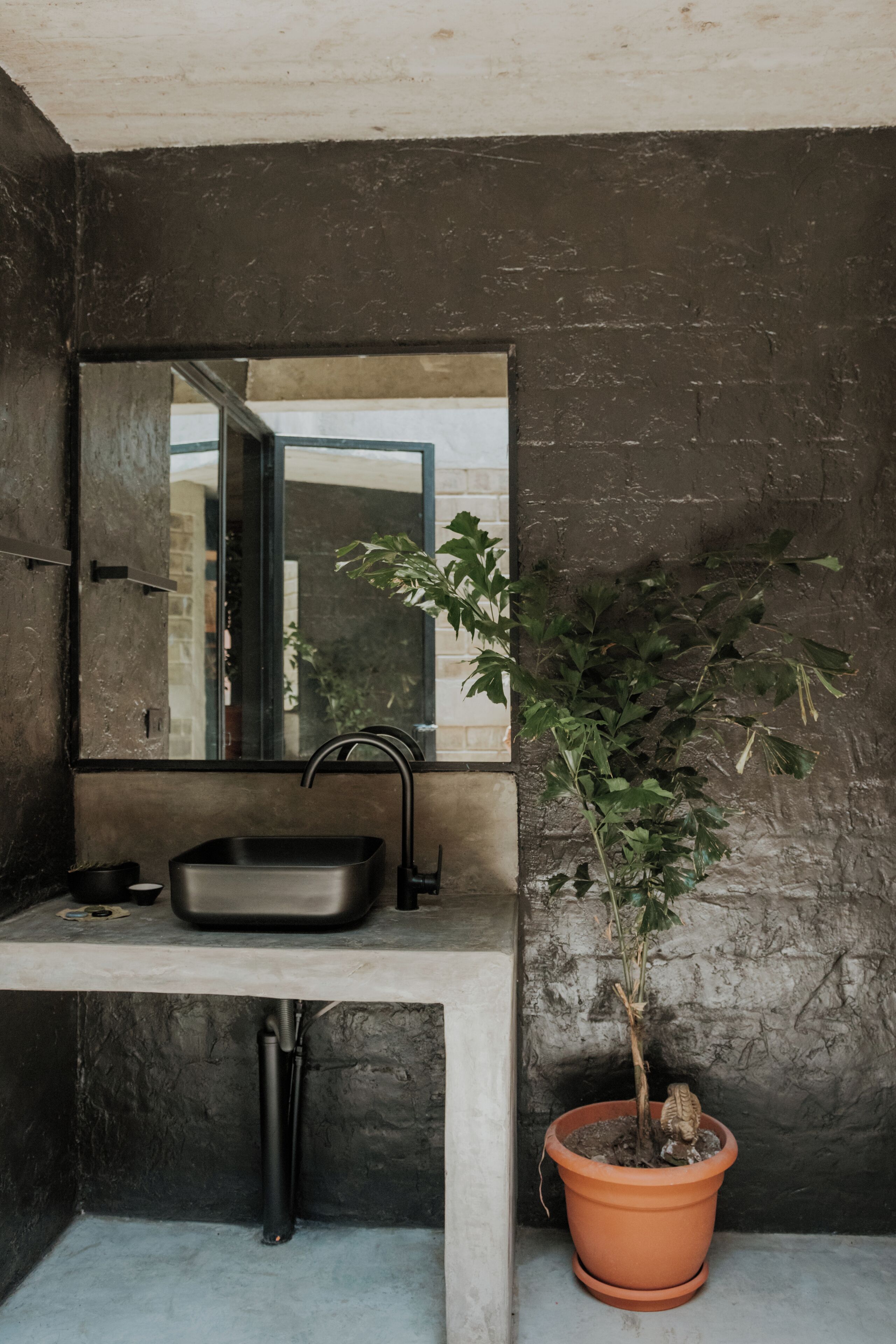 A modern bathroom with a rectangular sink, a large mirror, and a potted plant.