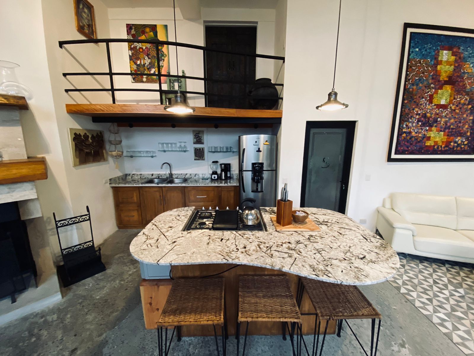 Une cuisine moderne dotée d’un îlot central, de tabourets en bois, d’une cuisinière encastrée et d’un réfrigérateur.