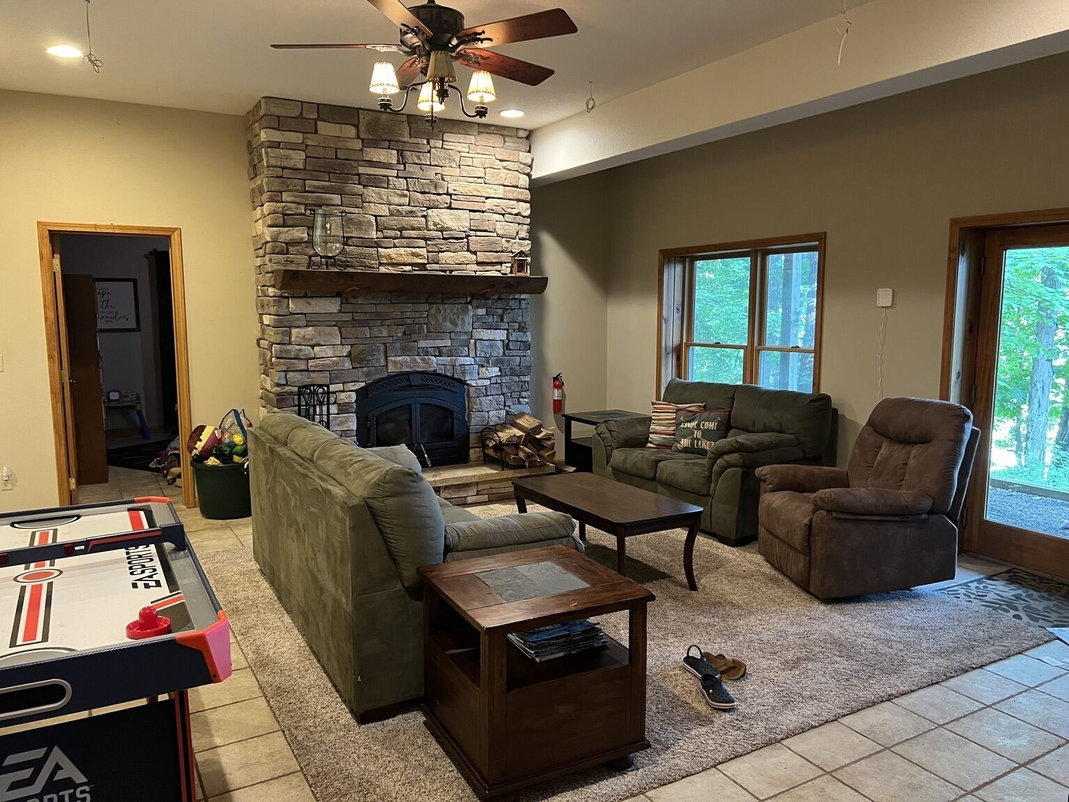 Un salon avec une cheminée en pierre, un ventilateur de plafond, un canapé, un fauteuil inclinable et une table basse.