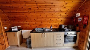 A compact kitchen with wooden walls, a sink, a stove, and cabinets. - Somerset glamping pod with access to adventure activities. (East Huntspill)