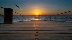 Eine Holzstege, der zum Meer führt, mit einem Sonnenuntergang im Hintergrund.