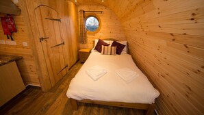 A wooden cabin bedroom with a bed, pillows, and a window.