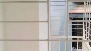 Un pasillo con barandilla metálica, una escalera y vista a un edificio con tejado de tejas.