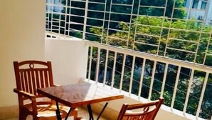 Un balcón con mesa y sillas, barandilla y vista a la vegetación a través de la barandilla.