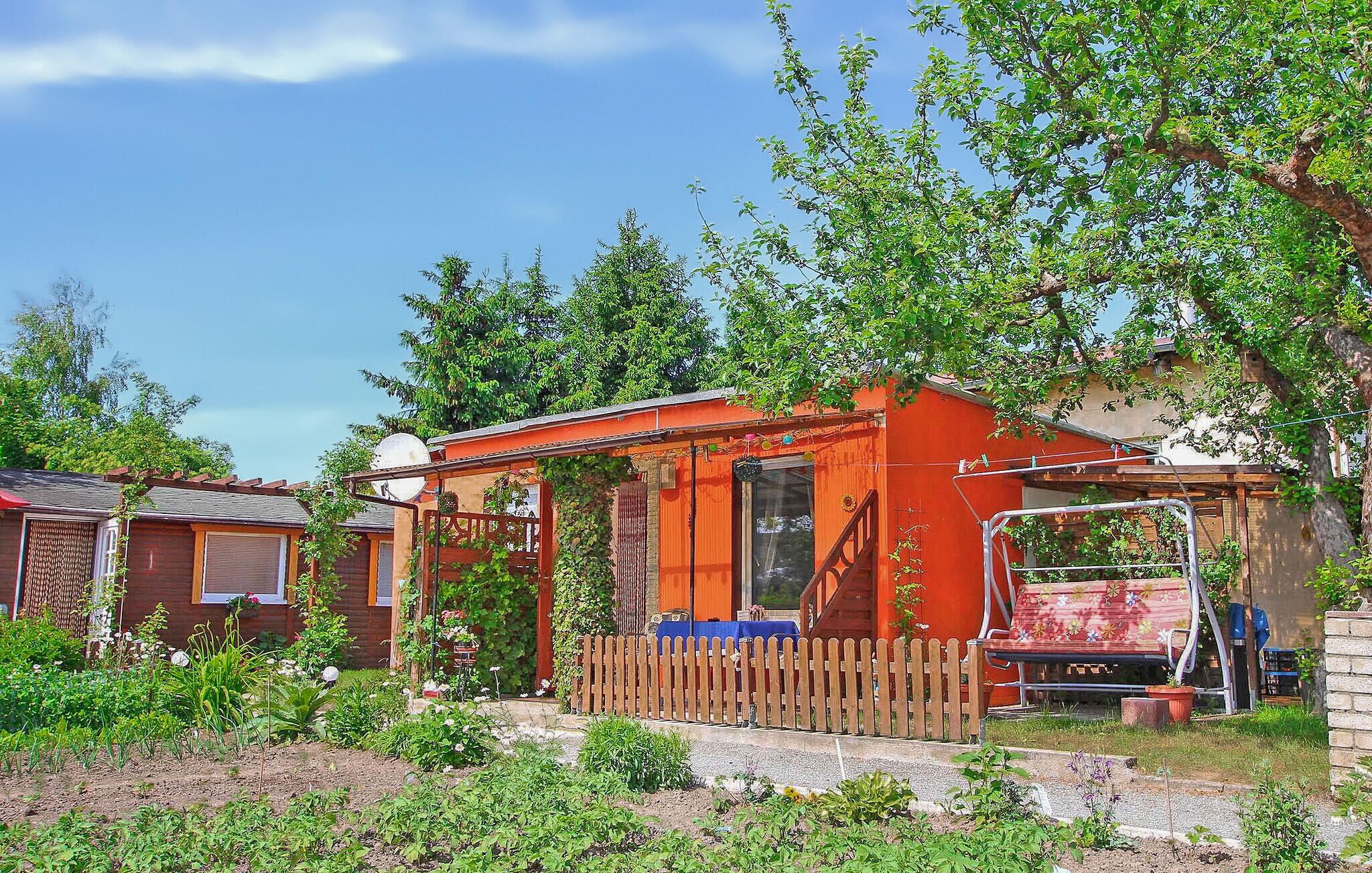 A small, single-story house with a red exterior, a wooden fence, and a garden in front.