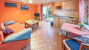 A living room with a sofa, a coffee table, and a television. There is a kitchen area with cabinets and a dining table. - Ferienwohnung Kölpinsee/Usedom (Kölpinsee/Usedom)