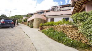 Une rue résidentielle bordée de maisons, avec une voiture garée et un mur de pierre recouvert de verdure.