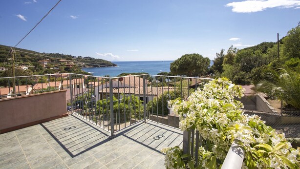 Un balcon avec vue sur la mer, un jardin agrémenté de fleurs blanches et un sol carrelé.