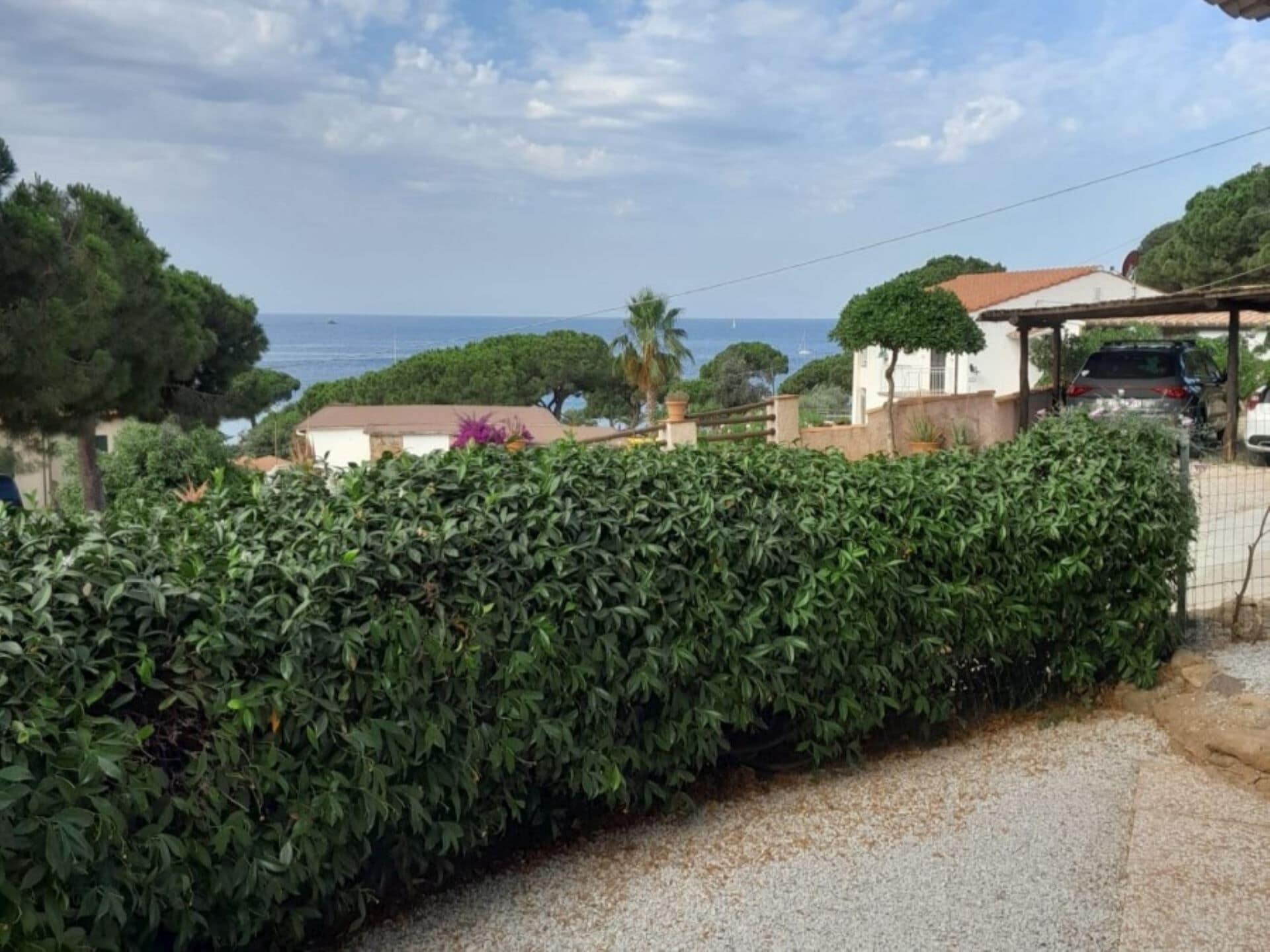 A residential area with a gravel driveway, a neatly trimmed hedge, and a view of the sea.
