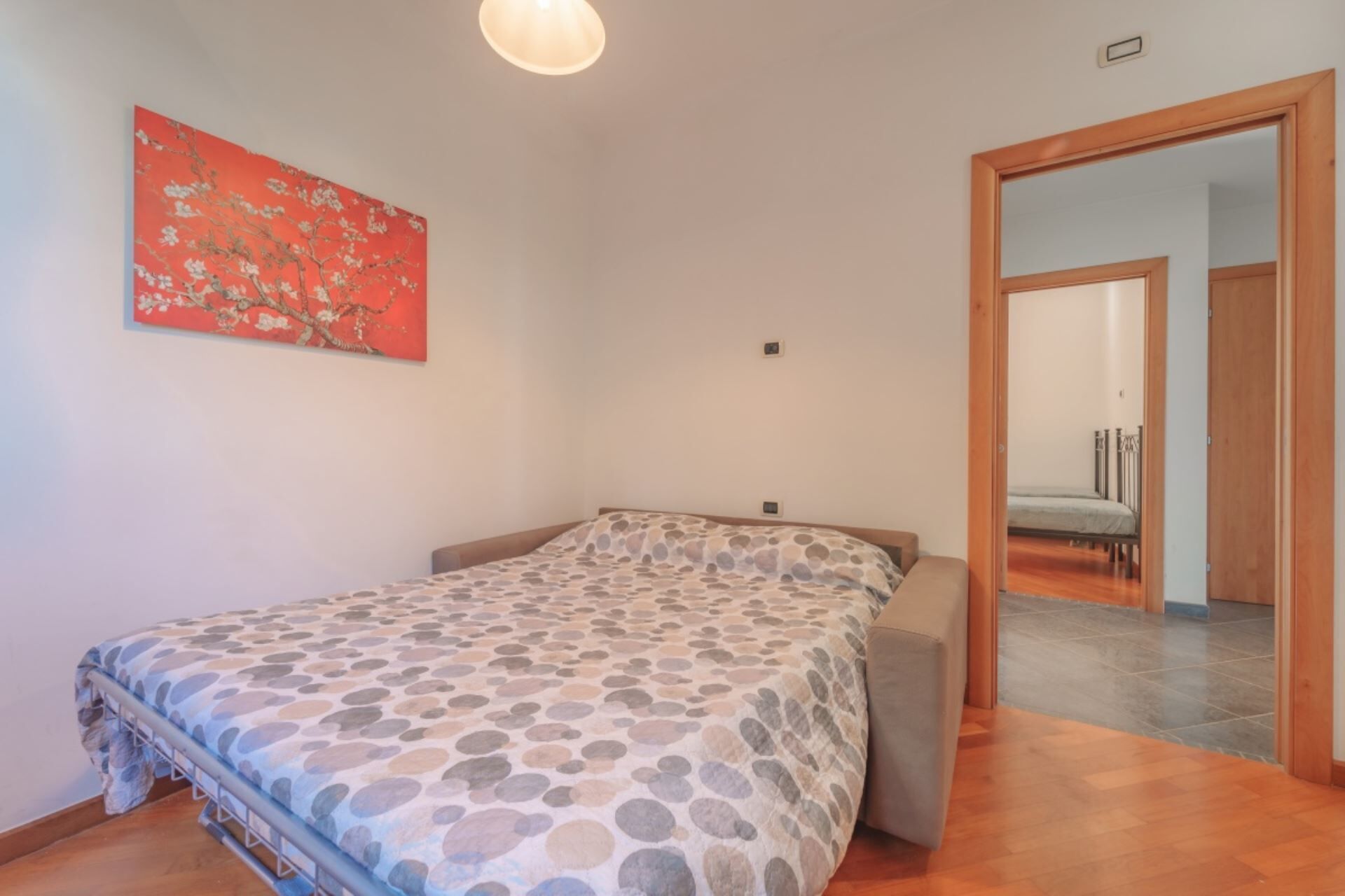 A bedroom with a bed, a door leading to another room, and a wall-mounted artwork.
