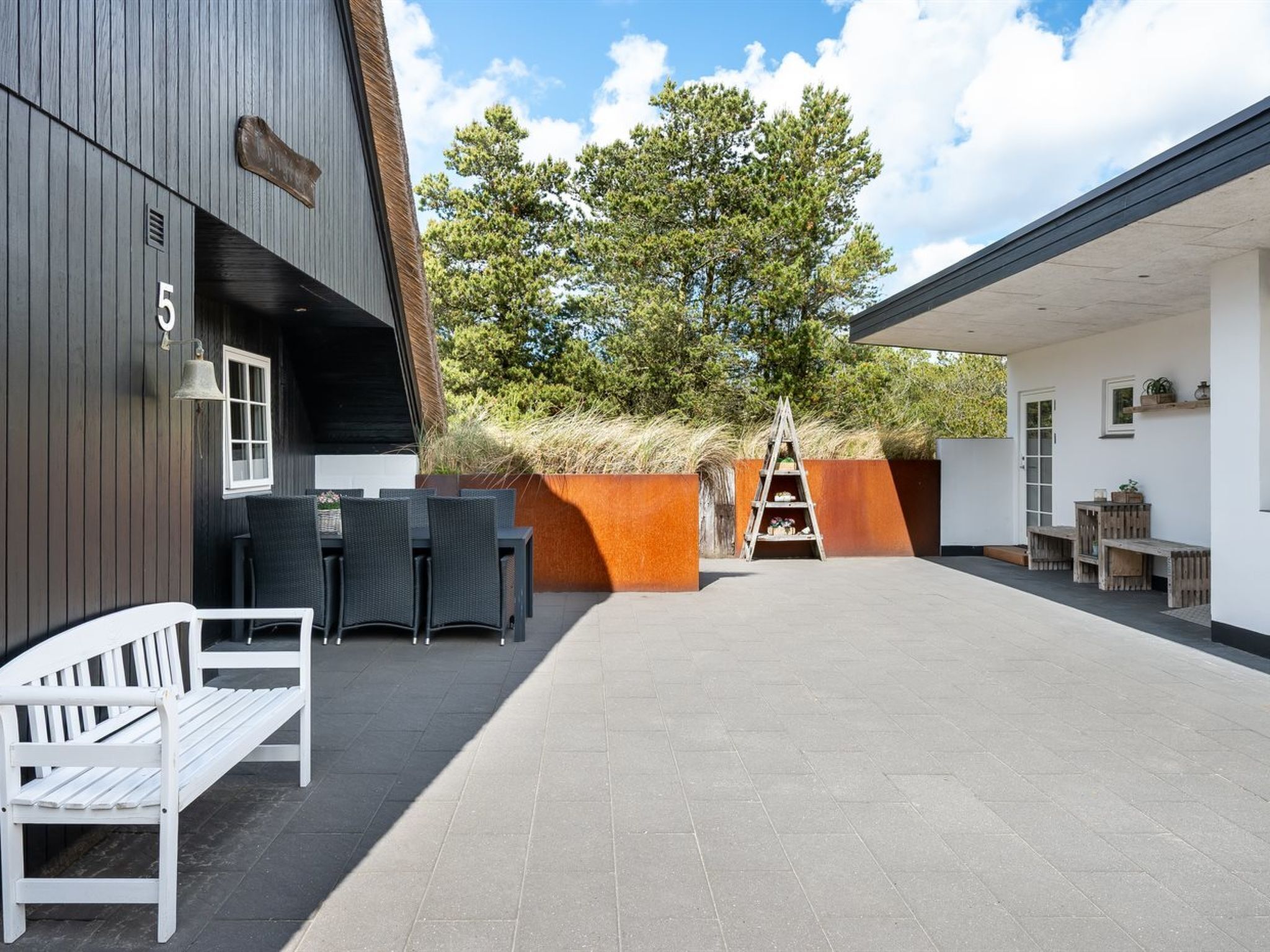 Un espace extérieur aménagé en patio, avec un banc en bois, une table et des chaises, et une échelle appuyée contre un mur.