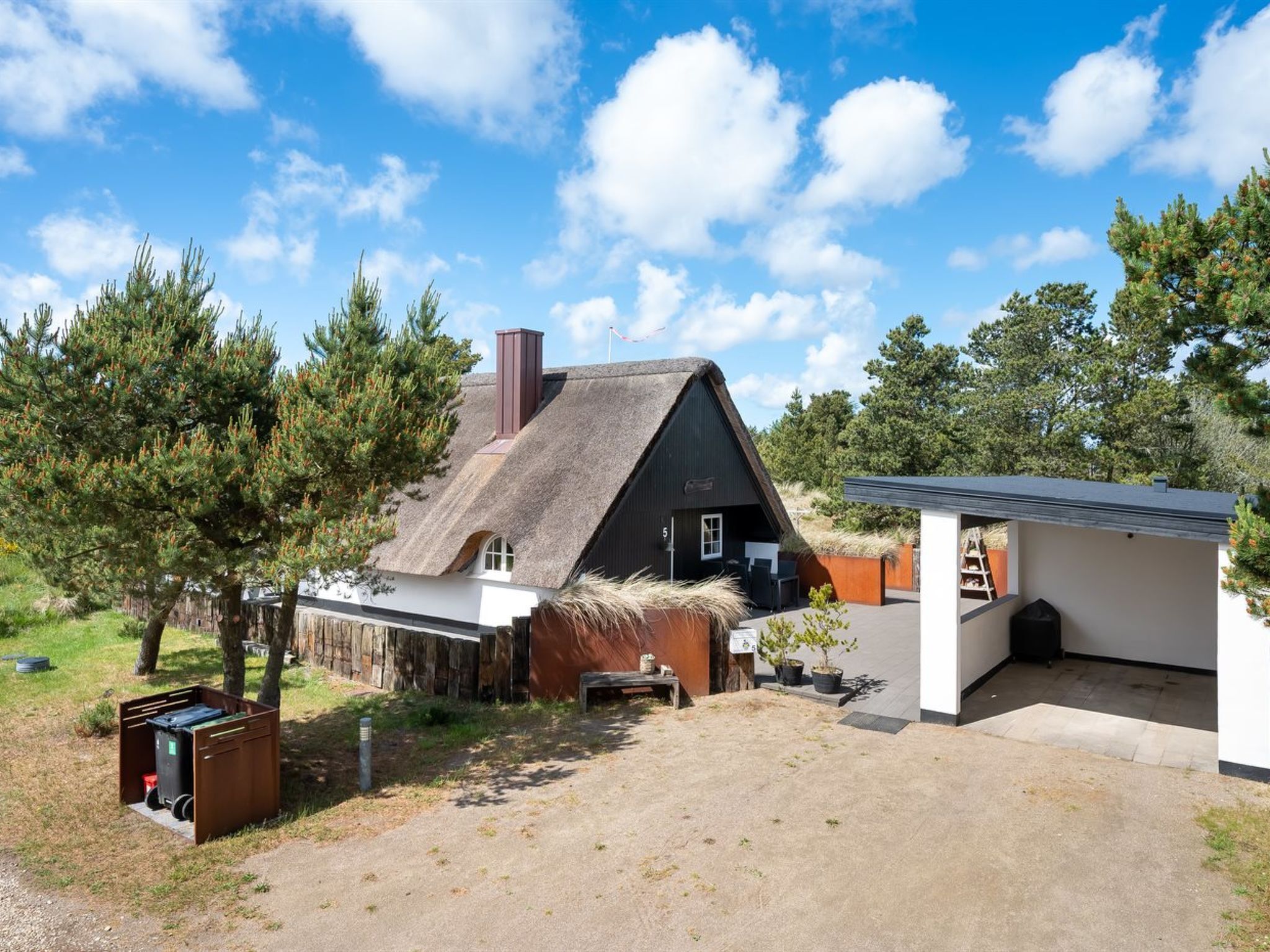 Une maison traditionnelle avec un toit de chaume, une petite dépendance attenante et une cour en terre battue.
