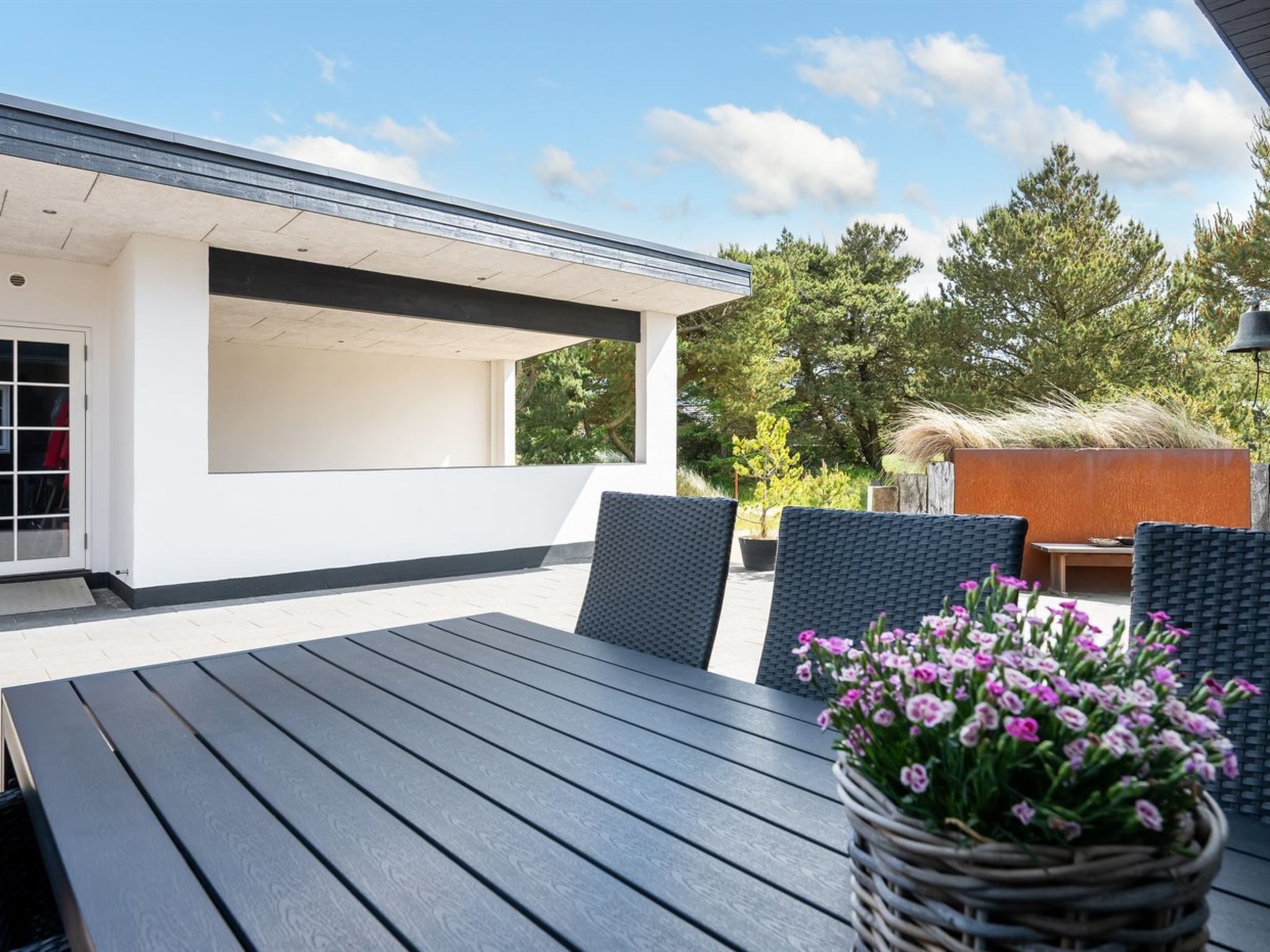 A modern outdoor patio with a wooden table, two chairs, and a potted plant.