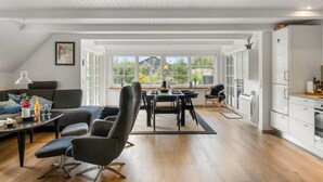 En rummelig opholdsstue med spisebord, sofaer og et køkken med hvide skabe.