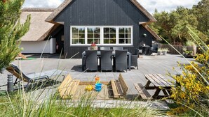 En moderne bygning med mørk facade, stort vindue og stråtækt tag.