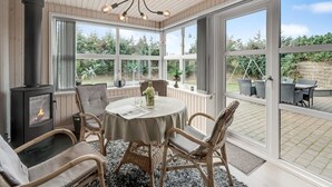 A cozy room with a round table, wicker chairs, a fireplace, and large windows offering a view of the garden. - "Geert" - 900m from the sea by Interhome (Blåvand)