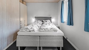A bedroom with a bed, a wardrobe, a bedside table, and a window with curtains. - "Geert" - 900m from the sea by Interhome (Blåvand)