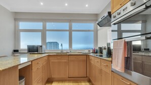 A modern kitchen with wooden cabinets, stainless steel appliances, and large windows offering a view of the cityscape. - Coastal Sunset By My Getaways (Brighton)