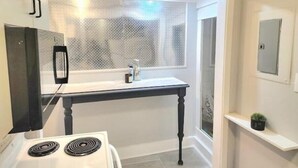 A compact kitchen with a stove, a small table, and a window with a frosted glass view. - 2 bed room Apartment (Albany)