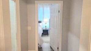 A hallway leading to a bedroom with a bed, nightstand, and lamp. - 2 bed room Apartment (Albany)