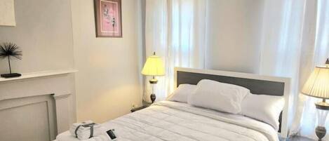 A neatly made bed with white bedding, a bedside lamp, and a framed picture on the wall.