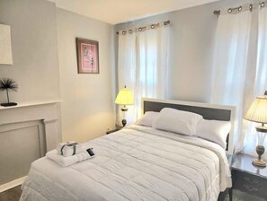 A neatly made bed with white bedding, a bedside lamp, and a framed picture on the wall. - 2 bed room Apartment (Albany)