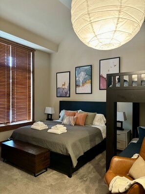 Ein Hotelzimmer mit Bett, Bank, Nachttisch, Lampe, Stockbett und Wandbild.