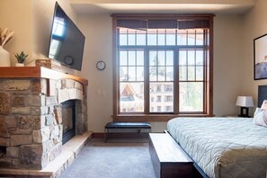 Un dormitorio con chimenea de piedra, un ventanal con vistas, una cama y un televisor montado en la pared.