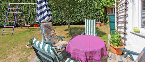 Une terrasse avec deux chaises à rayures, une petite table ronde recouverte d’une nappe rose et un parasol bleu et blanc à rayures.