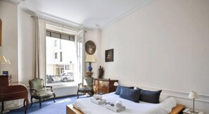 Hotelkamer met een bed, een stoel, een dressoir, een lamp en een raam met uitzicht op gebouwen en een fiets.