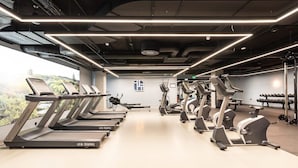 Ein Fitnessstudio mit mehreren Laufbändern und Crosstrainern, ein großes Fenster mit Blick auf Grünflächen und ein sauberes, modernes Design.