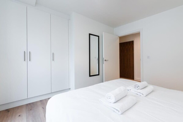 A hotel room with a bed, white wardrobe, and a door leading to another room.