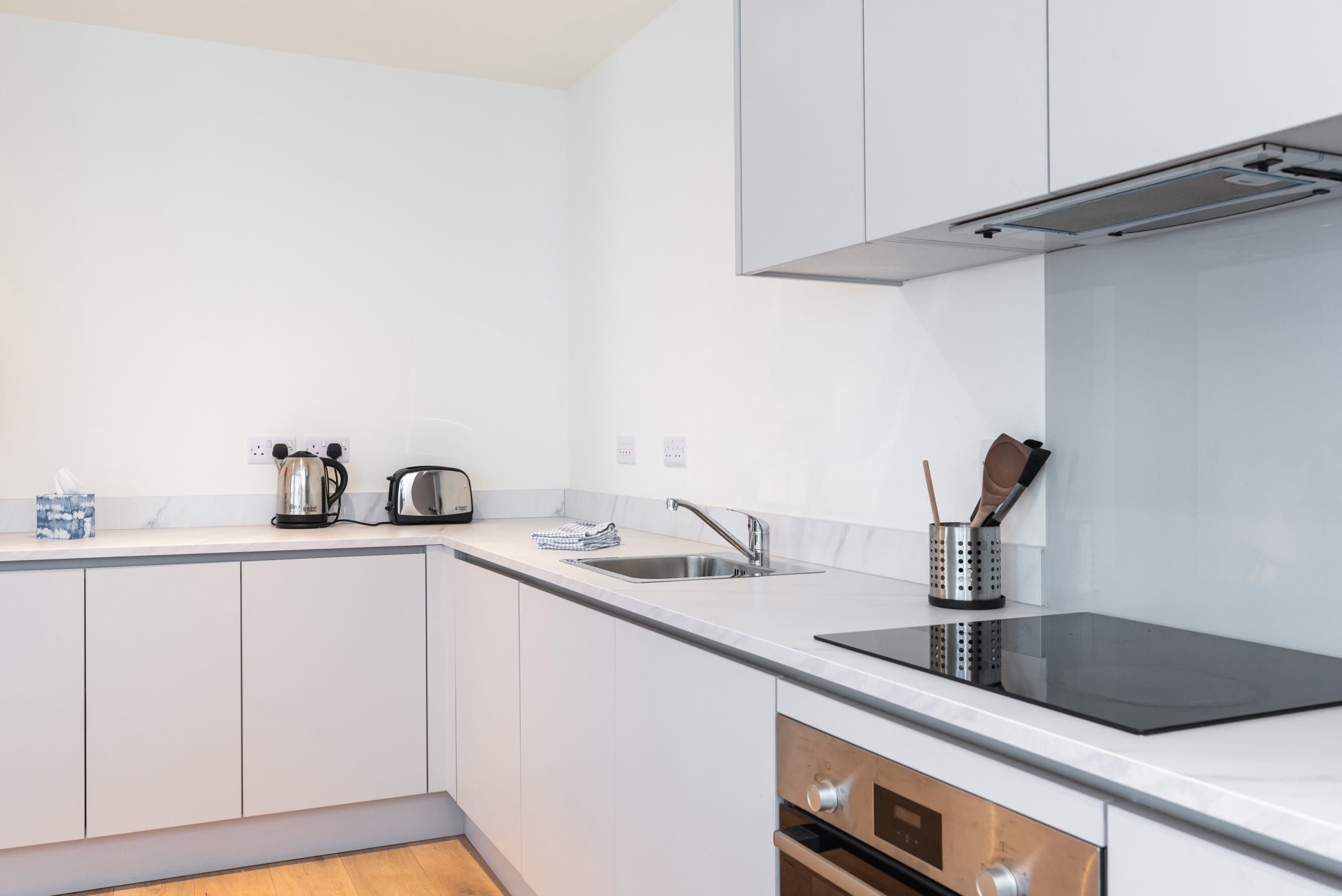 A modern kitchen with white cabinetry, a stainless steel sink, a black induction cooktop, and a built-in oven.