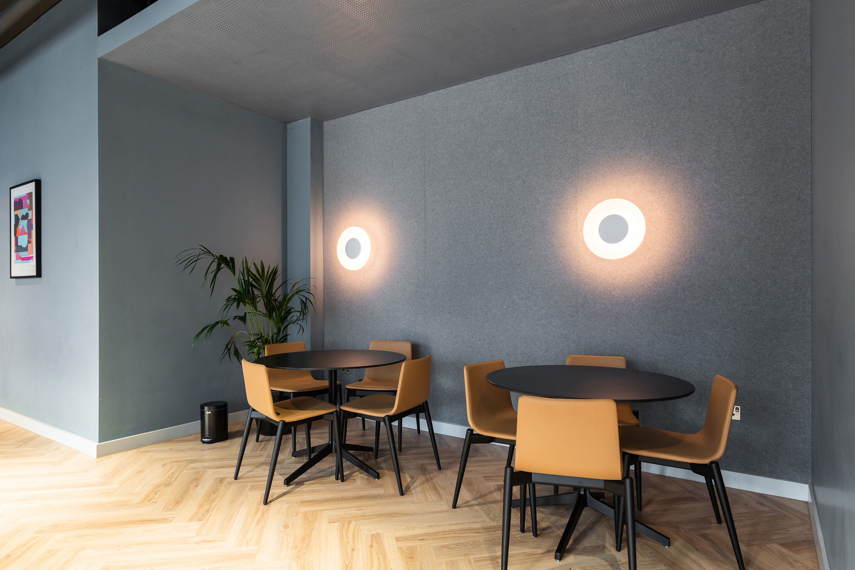 A modern conference room with two tables, chairs, and a potted plant.