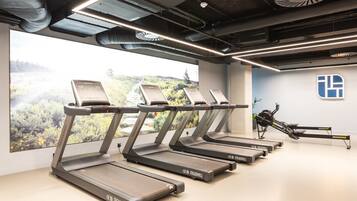 A gym with multiple treadmills, a rowing machine, and a large window with a view of a forested area.