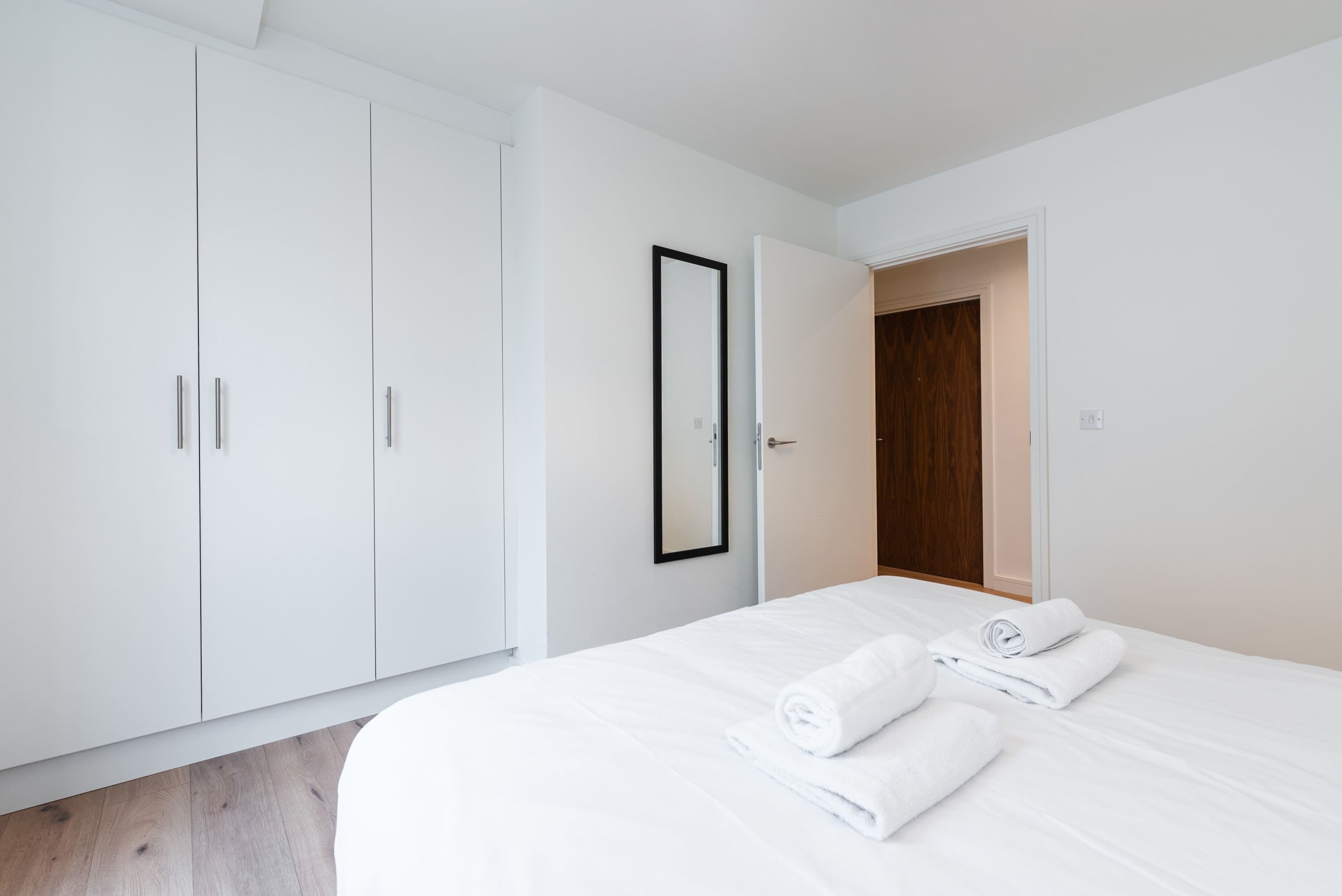 A bedroom with a large wardrobe, a bed with white linens, and a wooden door.