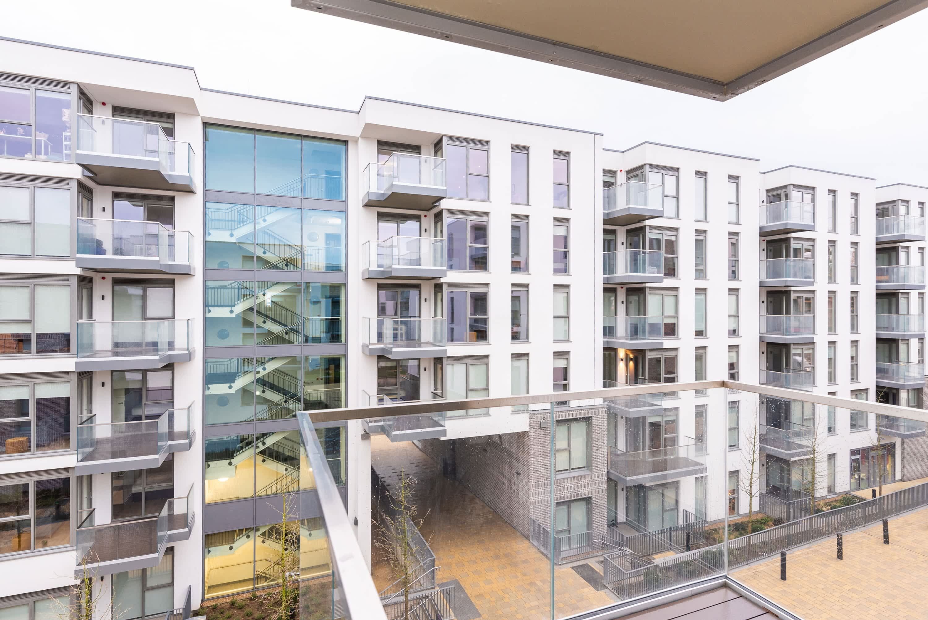 A multi-story residential building with balconies, a central staircase, and a glass facade.