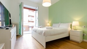 Un dormitorio con cama, mesitas de noche, cómoda y ventana con vistas a edificios.