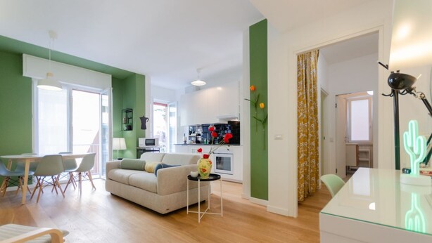 Una sala moderna con sofá, mesa de comedor y sillas. Se ve una cocina al fondo.