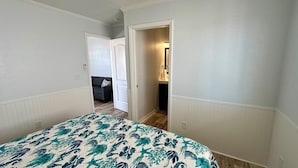 A bedroom with a bed, a door leading to a bathroom, and a hallway. - Fins Right - Next to Margaritaville (Fort Myers Beach)