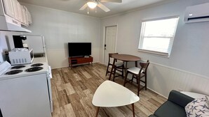 A compact kitchen with a stove, microwave, and a flat-screen TV. There's a dining table with two chairs and a sofa in the living area. - Fins Right - Next to Margaritaville (Fort Myers Beach)